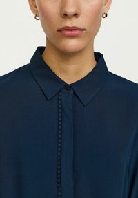 Marineblauwe button-up shirt met een klassieke kraag, voorzien van een gestructureerde voorkant met decoratieve details en een zachte stoftextuur.