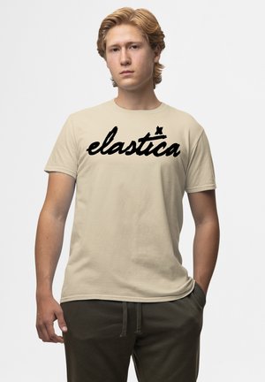 Beige bomulds t-shirt med et stort, fedt, sort skriftskrift logo "elastica" henover brystet. Korte ærmer, standard pasform.