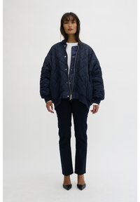 Navy quilted bomber jacket with ribbed cuffs and a gold zipper, paired with dark jeans and black pointed-toe heels. Smooth, glossy texture.
