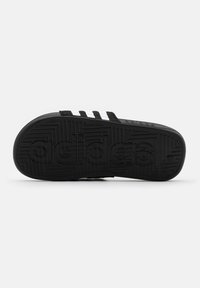 Czarna gumowa podeszwa sandała z trzema białymi paskami. Teksturowany wzór przyczepności z wytłoczonym logo 'adidas'. Płaski kształt, swobodny styl.