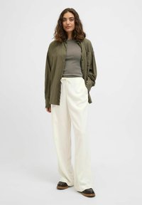 Chemise oversize vert olive à boutons, haut gris ajusté, pantalon large crème et chaussures marron à enfiler avec une semelle texturée.