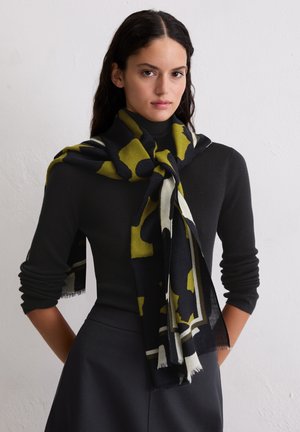 Sciarpa nera e verde con motivo, realizzata in tessuto morbido, drappeggiata con stile attorno al collo. I bordi presentano un delicato dettaglio di frange.
