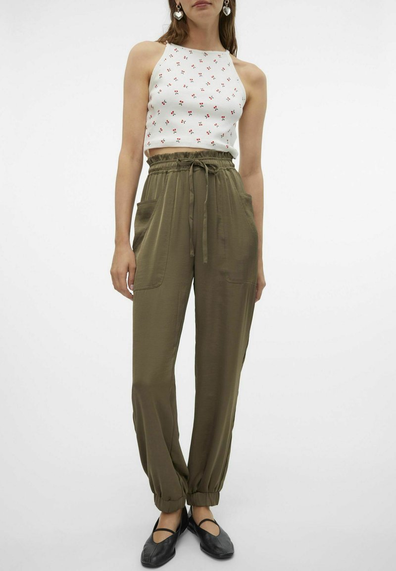 Top court blanc avec imprimé floral rouge, associé à un pantalon à taille élastique vert olive avec poches latérales et ourlets fuselés. Chaussures plates noires.