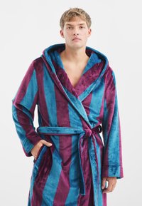 Pasiasty szlafrok w niebiesko-burgundowym pluszowym materiale; posiada kaptur, pasek oraz boczne kieszenie; miękka tekstura z kontrastującymi paskami.