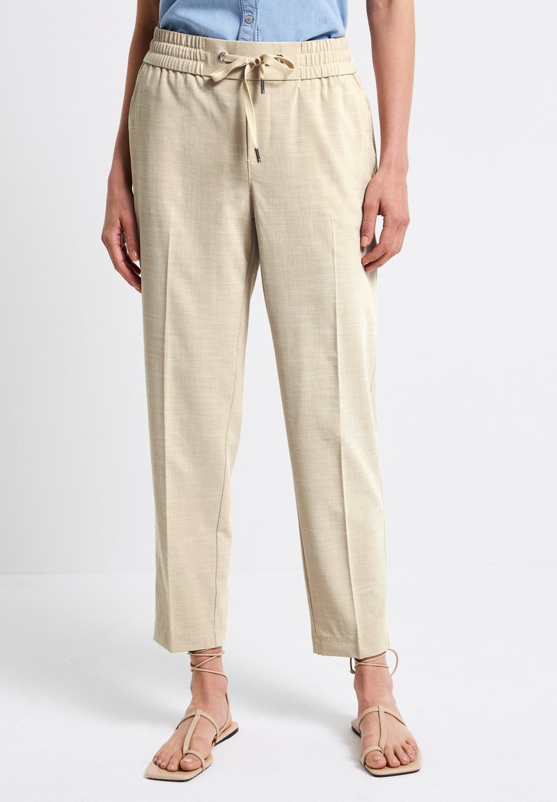 Beige, vävda byxor med elastisk midja och dragsko. Rak byxdesign, jämn textur, avvikande fåll, kombinerat med minimalistiska sandaler.