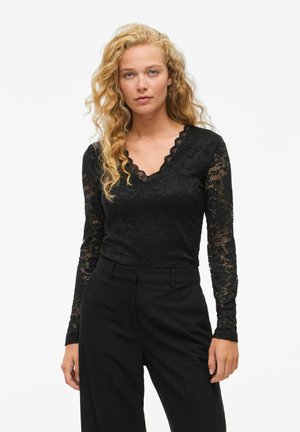 Zwarte kanten top met lange mouwen en bloemenpatroon, gegolfde V-hals, aangesloten taille, gecombineerd met zwarte, op maat gemaakte broek. Glad textuur.