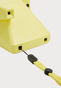 Yellow camera with a smooth matte finish, featuring a rectangular-shaped body and a textured grip, includes a prominent black cord attachment.