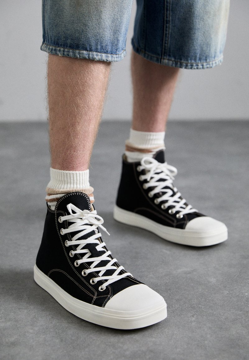 Sorte højtop sneakers med hvide snørebånd og gummitoe cap, parret med lette, ankel-længde strømper, båret med opsmøgte denim shorts.