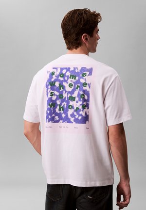 T-shirt blanc à manches courtes avec un motif graphique en violet et vert comprenant des éléments textuels, notamment des noms de villes en bas.