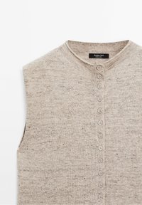 Gilet sans manches beige en tricot avec un col rond et une rangée verticale de petits boutons sur le devant.