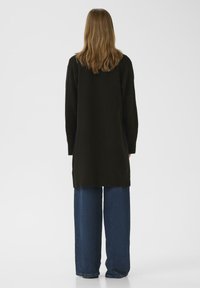 Black oversized sweater paired with wide-leg blue jeans. Sweater features a soft texture and long sleeves. Simple, minimalist design.