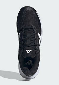 Czarny but sportowy z teksturowaną cholewką z siateczki, płaskimi sznurowadłami i trzema białymi paskami po bokach. Posiada zakrzywioną białą podeszwę.