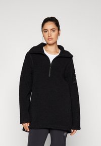 Pullover in pile nero con colletto a mezza zip, superficie texturizzata, maniche lunghe e tasca sul braccio sinistro. Vestibilità morbida e oversize.