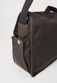 Bruine en zwarte stoffen schoudertas met een voorkant met drukknopvak en een zwarte verstelbare schouderband tegen een effen achtergrond.
