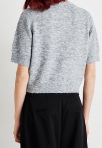 Gray, short-sleeved knit sweater with a soft texture and cropped design, featuring a ribbed hem and slightly fuzzy finish. Black trousers visible below.