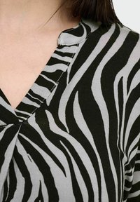 Svart och grått zebramönstrat tyg med V-ringning och synliga söm detaljer. Texturen verkar mjuk och lätt.