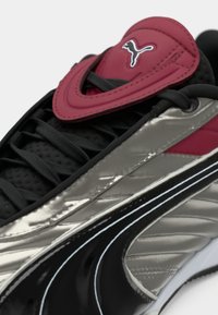 Gros plan d'une basket Puma noire et argent avec des lacets noirs et une languette rembourrée rouge arborant le logo blanc Puma.