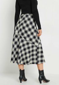Jupe midi à carreaux noir et blanc avec un design asymétrique, confectionnée dans un tissu léger. Portée avec des bottines noires.