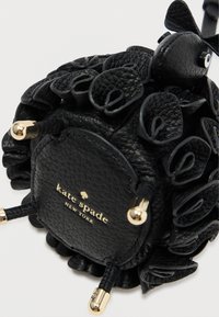 Czarna skórzana torebka z falbankowymi akcentami, złotymi dodatkami i zaokrąglonym kształtem. Wytłoczone logo na spodzie. Teksturalna powierzchnia.