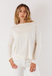 Maglia a maniche lunghe, leggera, di colore crema, con scollatura a barca e vestibilità morbida. Il materiale appare soffice con cuciture minime. Abbinata a pantaloni bianchi.