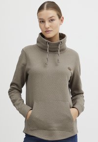 Pullover marrone chiaro con collo alto, lacci, motivo a pois e tasca a marsupio frontale. Materiale morbido con vestibilità rilassata.