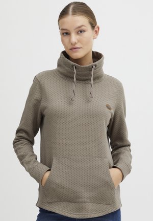 Pull léger marron clair avec un col montant, des cordons de serrage, un motif à pois et une poche avant. Matériau doux avec une coupe décontractée.