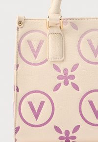 Cream faux leather handbag featuring a pattern of purple circles with "V" and floral designs. Includes a short handle and a textured finish.