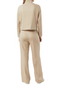 Beżowa krótka kurtka z wysokim kołnierzem, połączona z luźnymi spodniami z dopasowanego materiału. Gładka faktura, czyste linie bez ozdób.