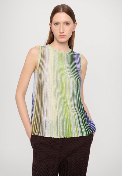 Top sin mangas multicolor con rayas verticales en verde, azul y crema, con textura acanalada. Combinado con pantalones oscuros con patrón de zigzag.