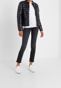 Black padded jacket with a zip closure, a round neckline, and a glossy texture, paired with slim dark jeans and white sneakers.