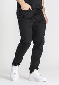Pantalones de mezclilla negros con un corte relajado, que presentan bolsillos laterales y costuras sutiles. Combinados con zapatillas blancas para crear contraste.