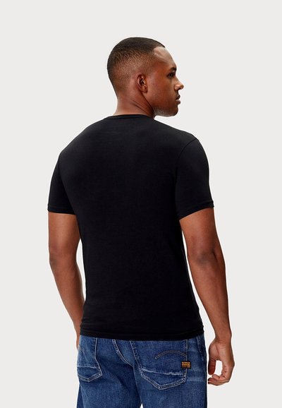 Czarny t-shirt z krótkim rękawem i okrągłym dekoltem, dopasowany krój o gładkiej fakturze, zestawiony z niebieskimi dżinsami z tylnymi kieszeniami.