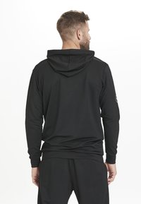 Sweatshirt à capuche noir à manches longues avec une coupe relax. Tissu lisse et léger. Présente un détail de logo sur la manche gauche.