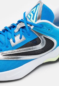 Blauer Sportschuh mit strukturiertem Obermaterial, silbernen Akzenten, schwarzem Netzpaneel und weißer Laufsohle mit minimalem Logodetail.