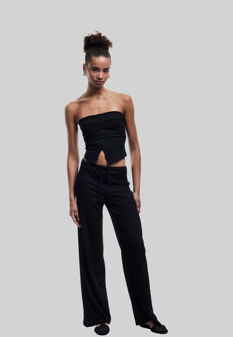 Sort stropløs top med struktureret stof og en forklaring, parret med sorte vide bukser og sorte slip-on sko med udskæringer.