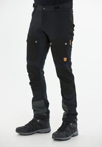 Pantalons de plein air noirs avec plusieurs poches, genoux renforcés, tissu texturé contrastant et un petit logo en patch sur la cuisse.