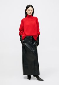 Punainen poolopaita, jossa on ribattu kaulus, yhdistettynä pitkään mustaan nahkahameeseen. Mustat nahkakintaat ja teräväkärkiset mustat korkokengät täydentävät asustusta.