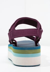 Sandalo con cinturino in tessuto viola con una spessa suola piattaformata multicolore in blu, verde, azzurro e bianco, mostrato da dietro.