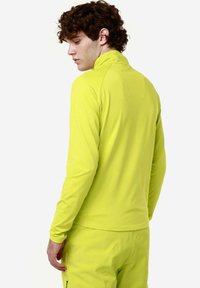 Pullover a maniche lunghe e collo alto di un vivace giallo. Tessuto liscio e elasticizzato con maniche aderenti. Cuciture minime e nessun logo o accento visibile.