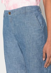 Pantalones de mezclilla de color azul claro con una textura suave, cierre de botón y bolsillos delanteros. La tela tiene un aspecto ligeramente desgastado.