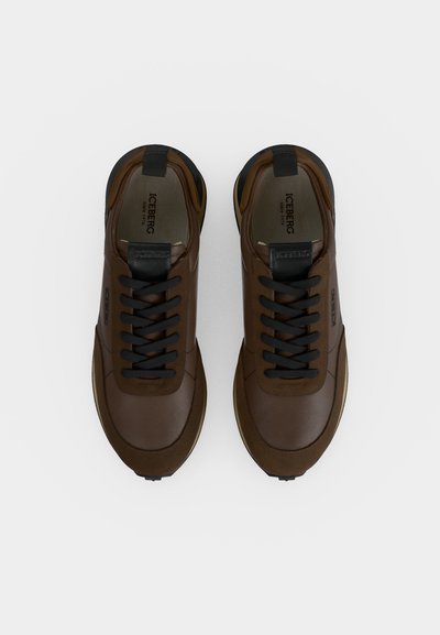 Paire de baskets en cuir marron avec des lacets noirs et des détails noirs, vues de dessus sur un fond blanc uni.