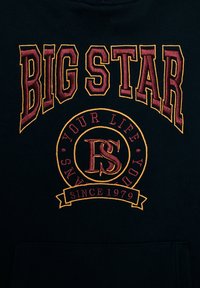 Sudadera negra con texto bordado: "BIG STAR" en color burdeos, logo circular con "YOUR LIFE" y "SINCE 1979" en acentos dorados.