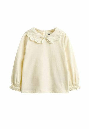 Kremfarvet babybluse med lange ærmer, scallop-lace krave og lille sløjfe, med elastiske manchetter på ærmerne.