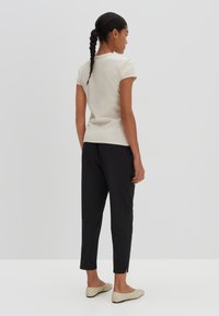 Top a maniche corte ribbed beige chiaro abbinato a pantaloni neri tapered e scarpe slip-on beige, presentato da dietro su uno sfondo neutro.