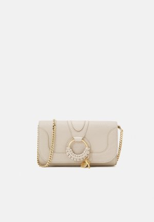 Beige leren crossbodytas met een gevlochten gouden ring als hardwareaccent, een getextureerd oppervlak en een kettingriem.