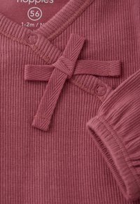 Nahaufnahme eines gerippten rosa Babywickelsweaters mit Schleifendetail, Druckknöpfen und Größenlabel 56 für 1-2 Monate alte Babys.