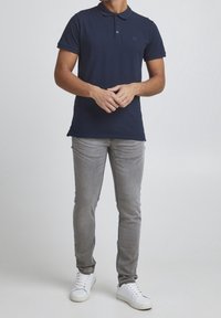 Granatowa koszulka polo z klasycznym kołnierzykiem, zestawiona z jasnoszarymi jeansami o dopasowanym kroju i białymi trampkami. Prosty design, miękka tkanina.