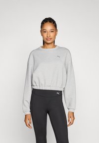 Sudadera corta gris con un acabado texturizado y borde inferior elástico, combinada con leggings negros que presentan un pequeño logo en la cinturilla.