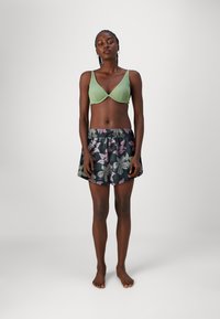 Lys grøn ribbet bralette og sort skjørt med fargerik blomstermønster. Skjørtet har elastisk midjebånd og er knelangt. Flate føtter synlige.