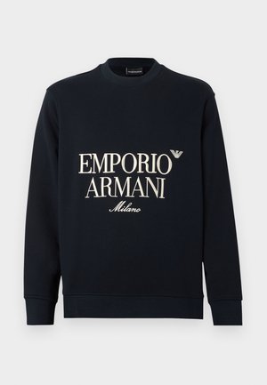 Granatowa bluza z długimi rękawami, okrągłym dekoltem i gładką fakturą tkaniny. Z przodu znajduje się biały napis "EMPORIO ARMANI" oraz logo "Milano".